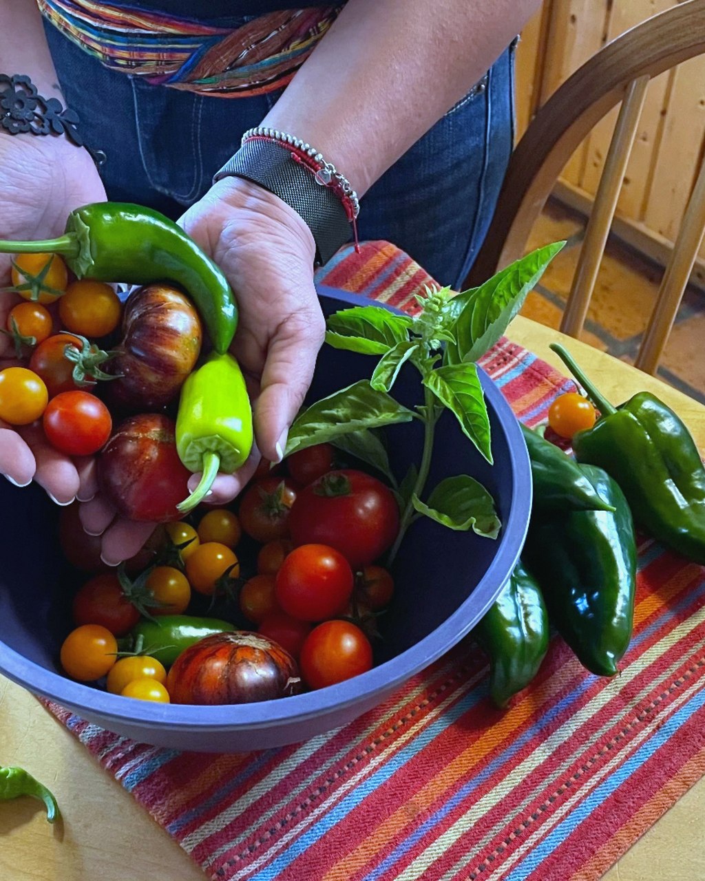 Hands holding freshly picked tomatoes and peppers over a bowl of produce