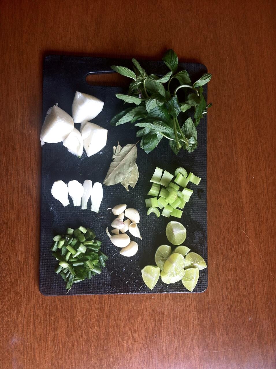 Onion, garlic, mint, celery, scallion, and lime arranged on a cutting board